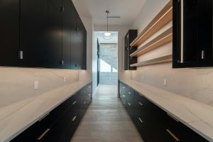 A long modern pantry with dark cabinetry and stone counters
