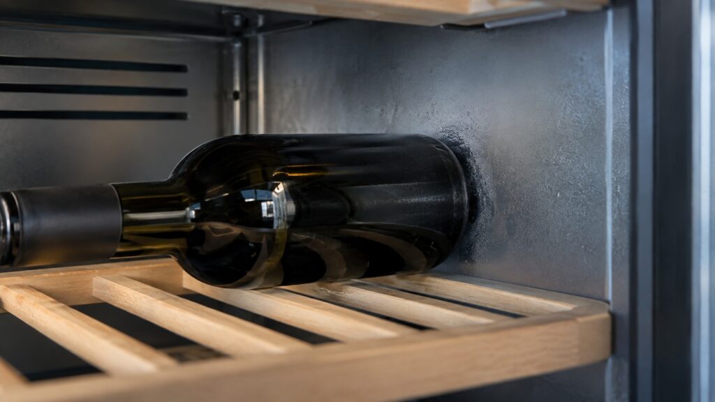 A close-up of a wine bottle touching the cold rear wall inside a wine cabinet