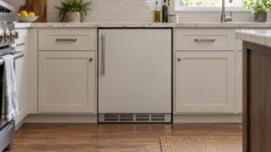 A built-in undercounter cabinet between two kitchen base cabinets with a vented panel at its base