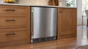 A built-in undercounter refrigerator with its vented base grille visible between wooden cabinets